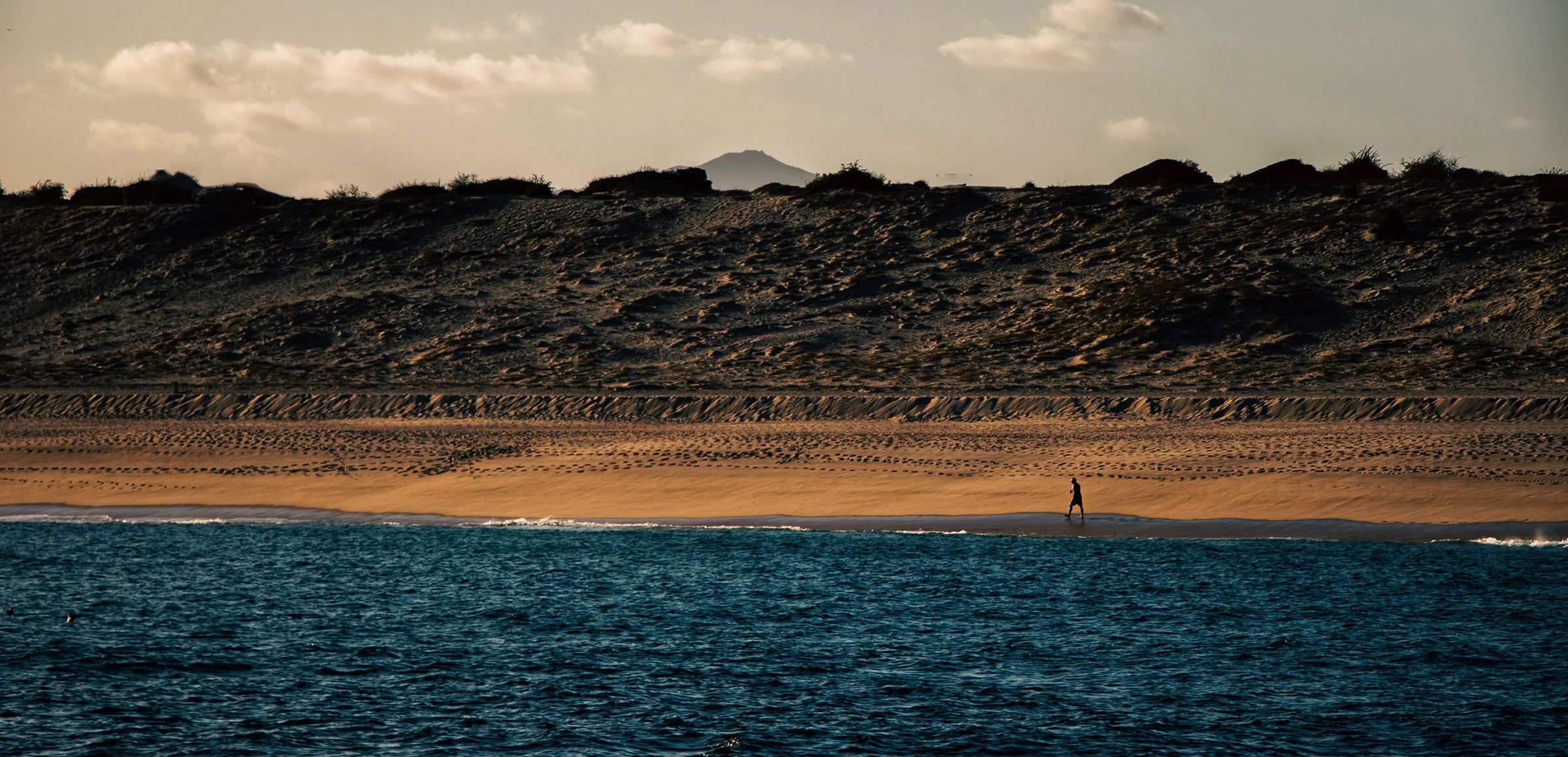Litoral abierto del Pacífico al final del día, con una figura caminando por la duna.